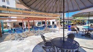 An outdoor pool area with seating arrangements, including tables and chairs, under a covered pergola. - Aquarius Flat Service (Caldas Novas)