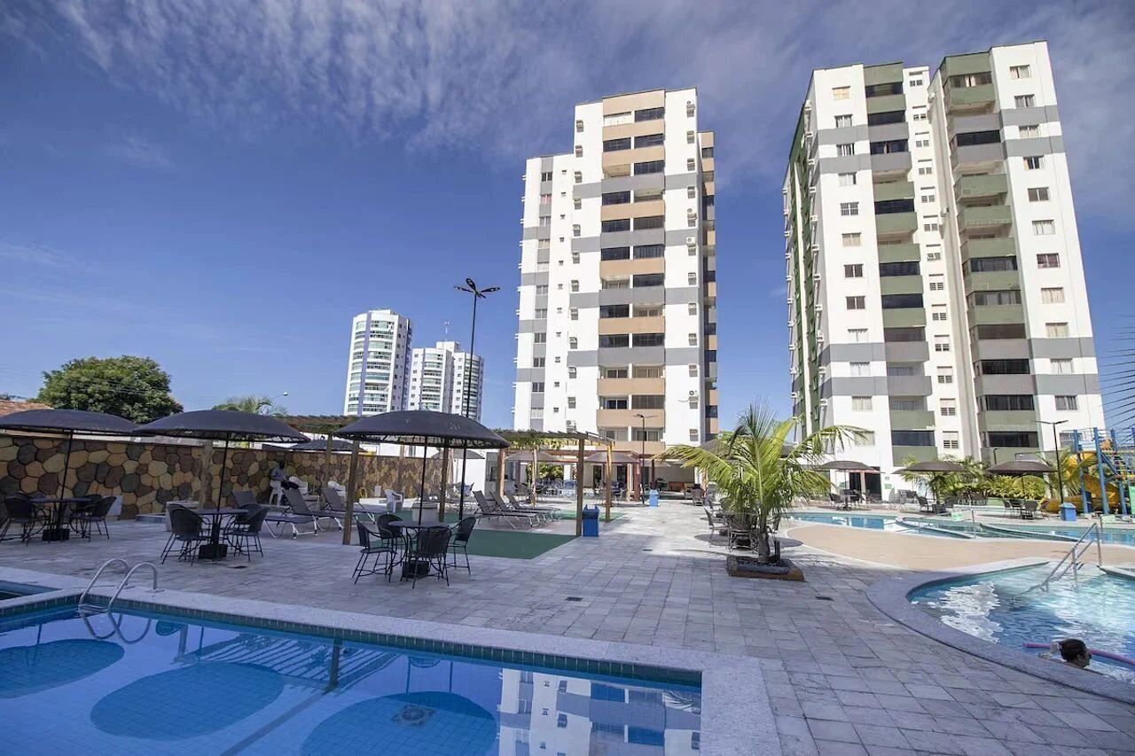 Un espace piscine d’hôtel avec des chaises longues et des parasols, entouré de grands immeubles.