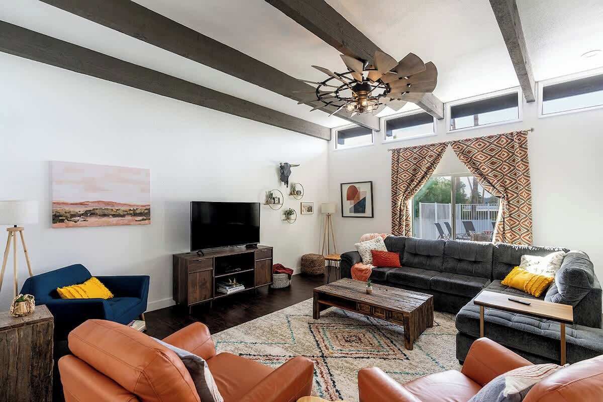 Una sala de estar con un sofá oscuro, un sillón azul, una mesa de centro de madera y un televisor.