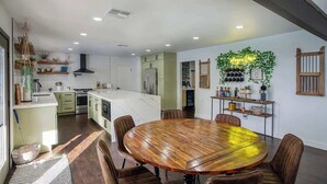 A modern kitchen with a central island, dining area with a wooden table and chairs, and a wall-mounted wine rack.