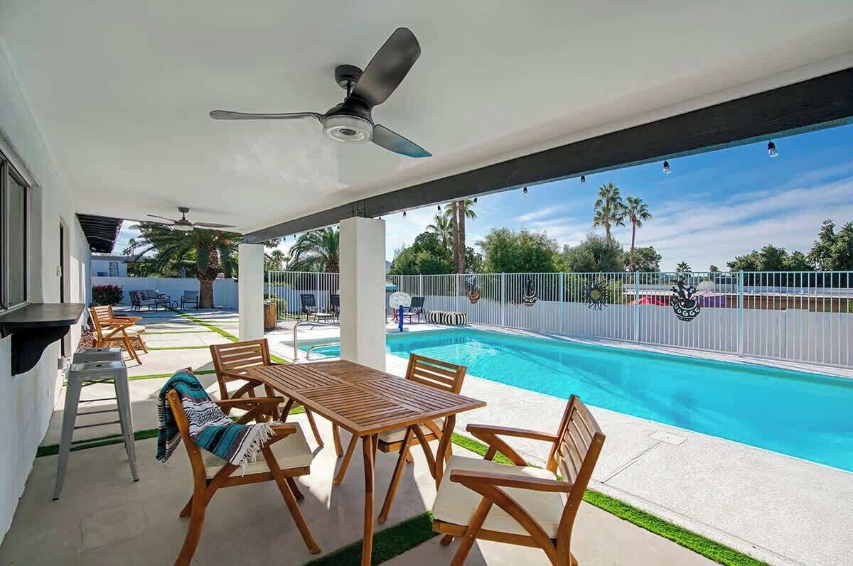 Un espacio al aire libre techado con piscina, muebles de madera y un ventilador de techo.