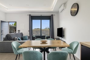 Un salon moderne comprenant un canapé, une table à manger et des chaises, un téléviseur et une grande fenêtre avec des rideaux.