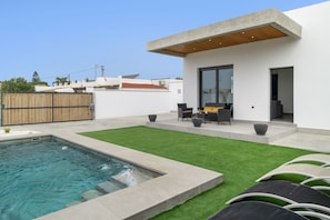 A modern outdoor pool area with a built-in hot tub, a patio with seating, and a well-maintained lawn.