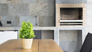 A wooden table with a woven basket containing green plants, a stone wall, and a brick oven in the background. - Guest House 'Jazmin' with Private Pool, Wi-Fi and Air Conditioning (Conil de la Frontera)