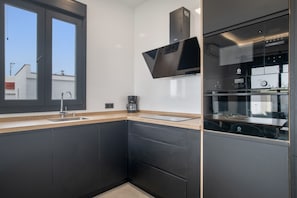 A modern kitchen with dark cabinetry, a stainless steel sink, a coffee maker, and a built-in oven.