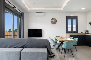 Un salon moderne comprenant un canapé, un téléviseur à écran plat, une table à manger avec des chaises, et un coin cuisine avec un évier et des placards.