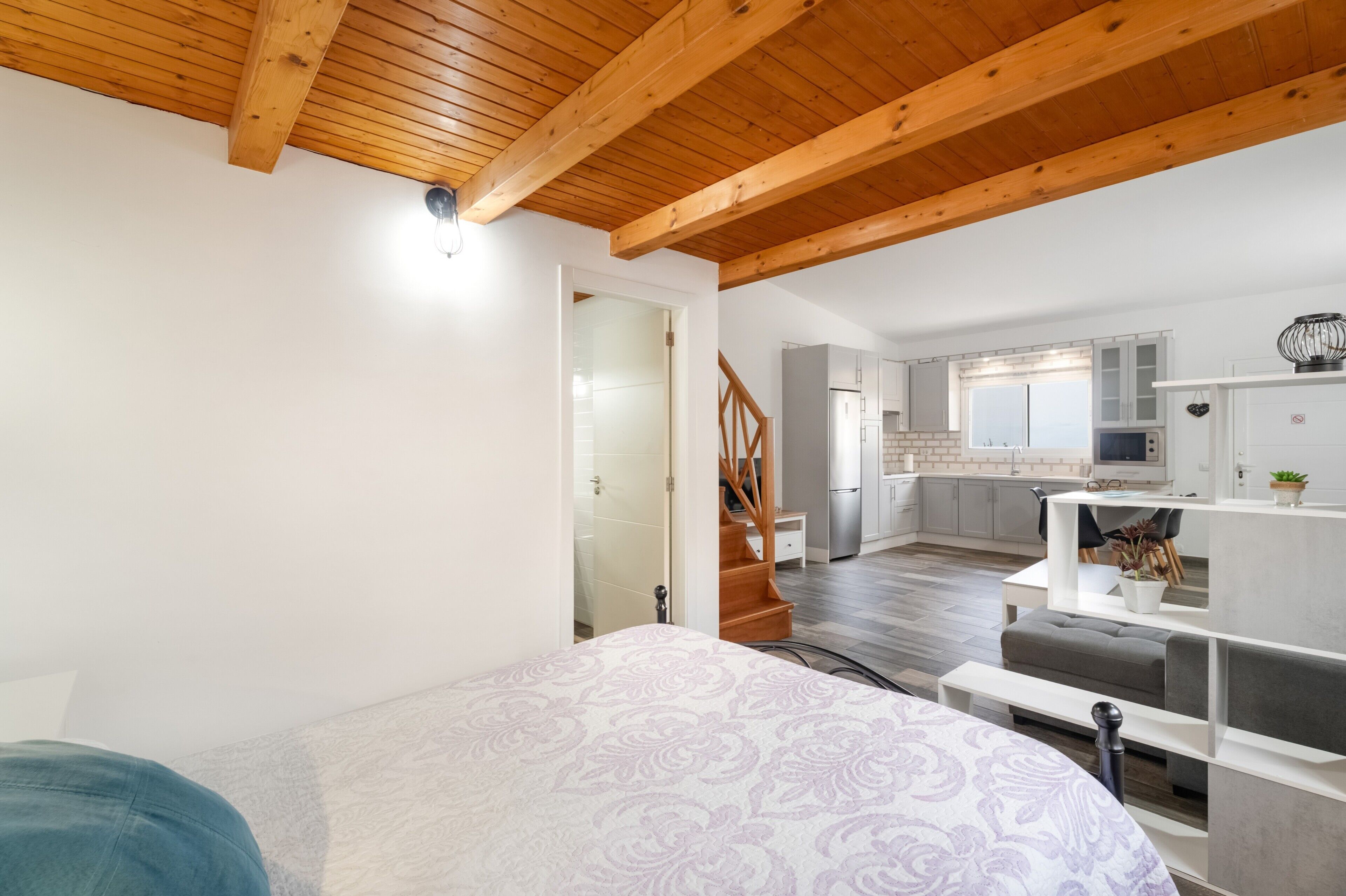A bedroom with a bed, a staircase leading to a kitchen, and a dining area.