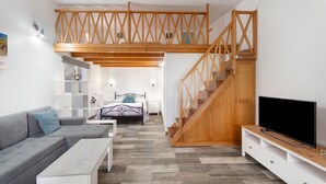 A modern living room with a sofa, coffee table, TV stand, wooden staircase, and a bed with a headboard. - Studio 'De Tato' with Mountain View, Private Terrace and Wi-Fi (La Frontera)