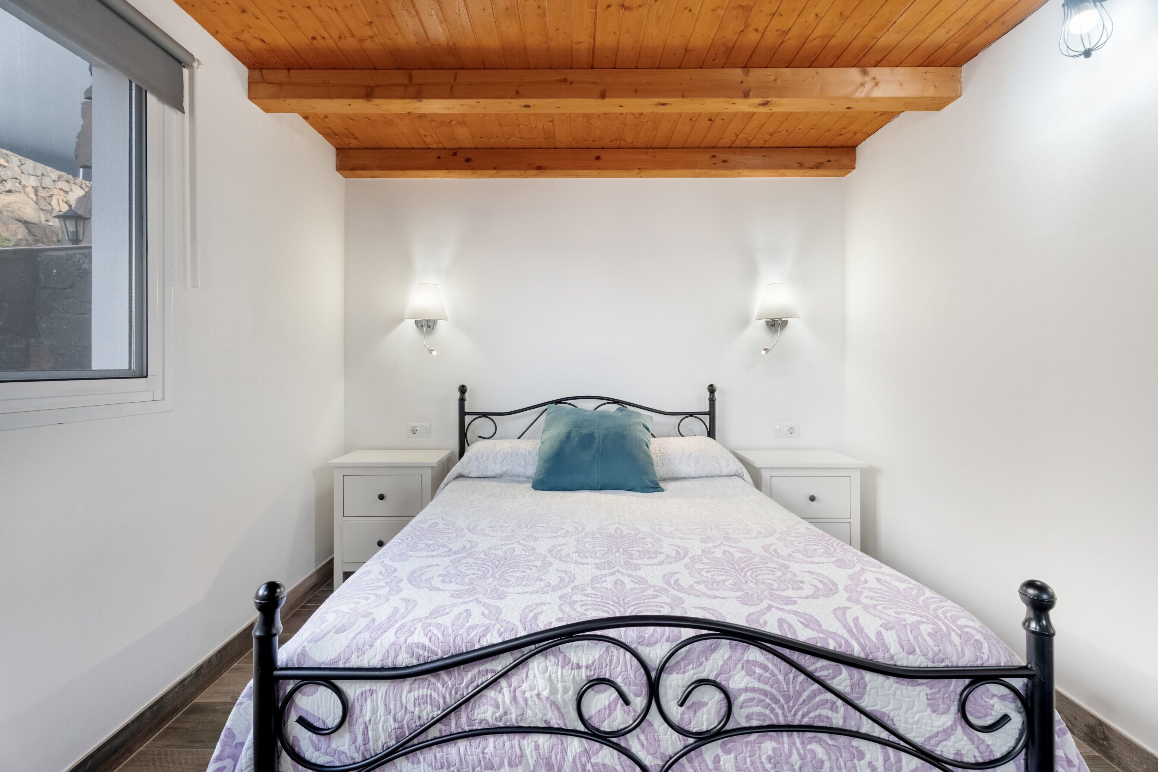 Une chambre à coucher avec un lit, deux tables de chevet, une fenêtre et un plafond en bois.