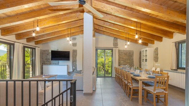 Une salle à manger spacieuse avec une longue table en bois, de nombreuses chaises et un ventilateur de plafond.