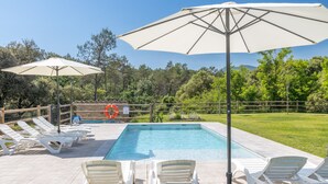 Une piscine entourée d’une clôture et d’arbres, avec des chaises longues et des parasols.