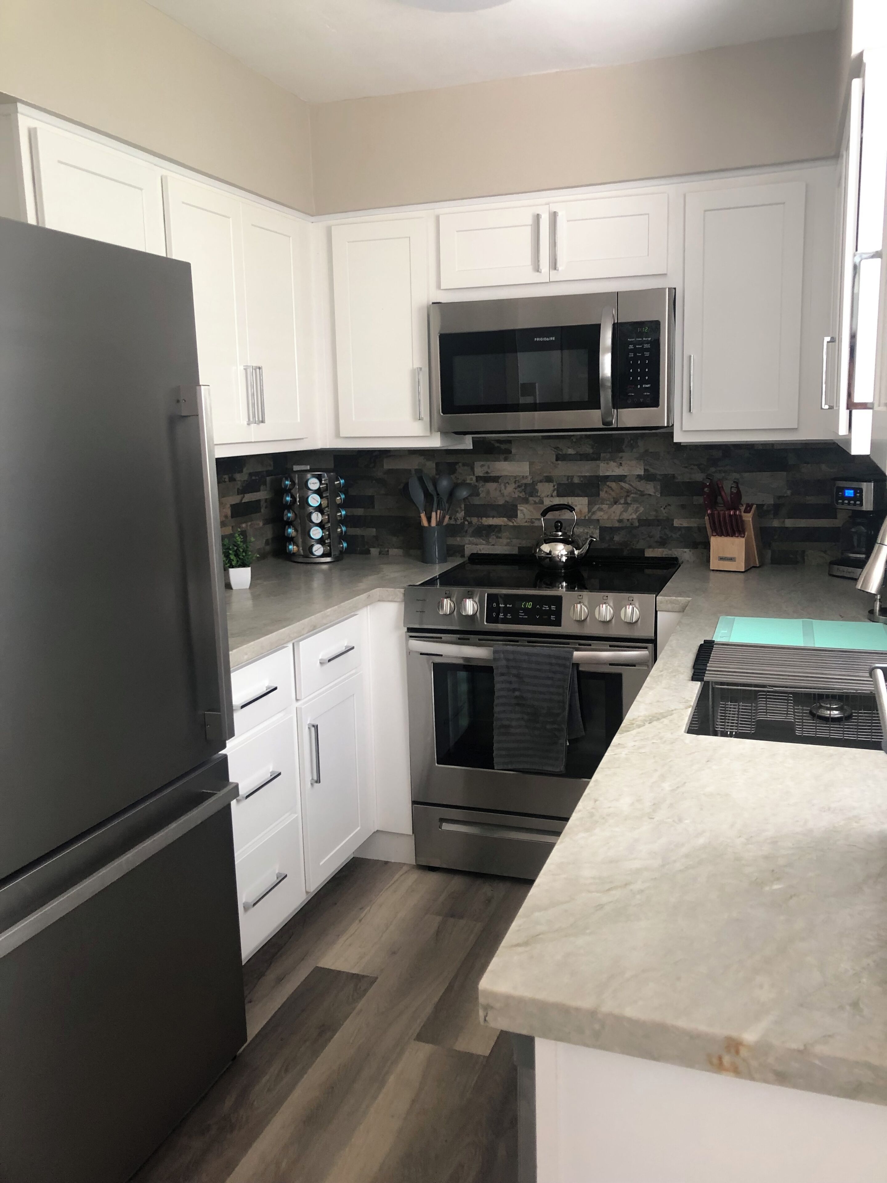 A modern kitchen with white cabinets, stainless steel appliances, and a wooden floor.