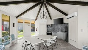 A spacious indoor area with a large table and chairs, a kitchen with modern appliances, and a view of the outdoors.
