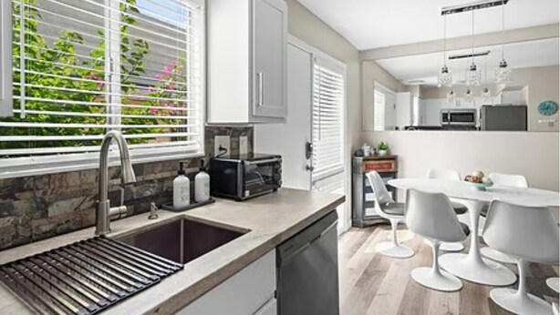 A modern kitchen with a built-in dishwasher, a double sink, and a dining area with a white table and chairs.