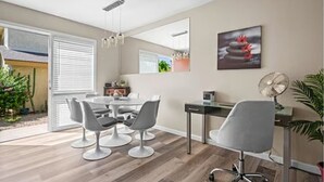 A modern dining area with a table and chairs, a large window with blinds, a ceiling fan, and a wall-mounted artwork.