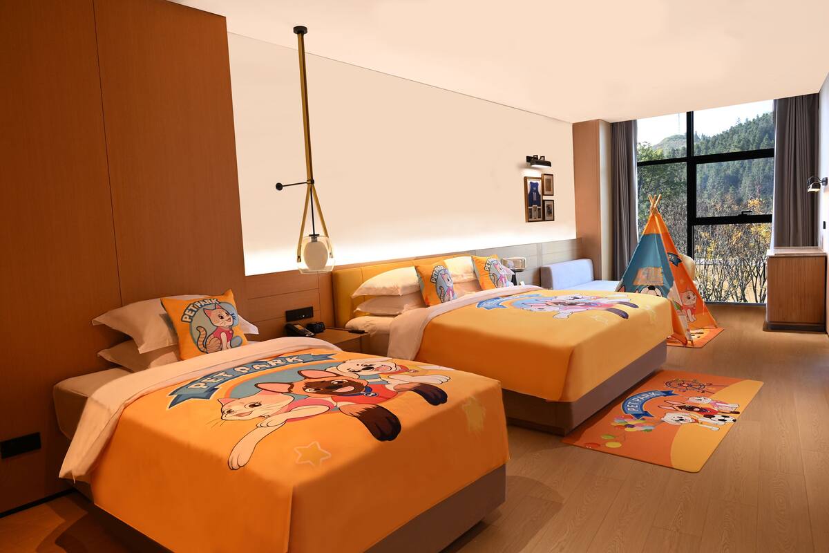 Une chambre d’hôtel avec deux lits, chacun recouvert d’une couvre-lit à motifs de dessins animés, une fenêtre donnant sur des arbres et un plancher en bois.