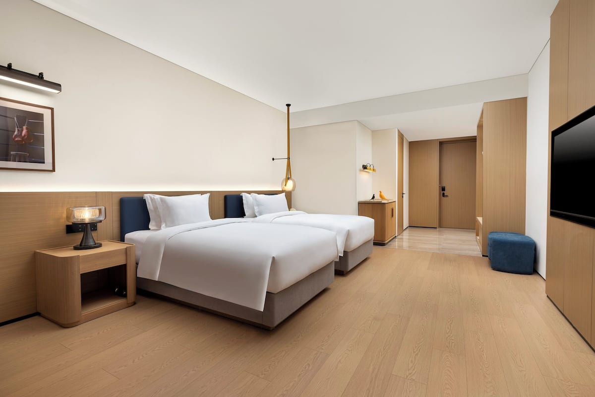 Une chambre d’hôtel moderne équipée de deux lits, d’une télévision et d’un petit bureau avec une lampe.