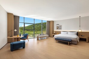 Een moderne hotelkamer met een groot raam, een bank, een bed, een bureau en een zitbankje.