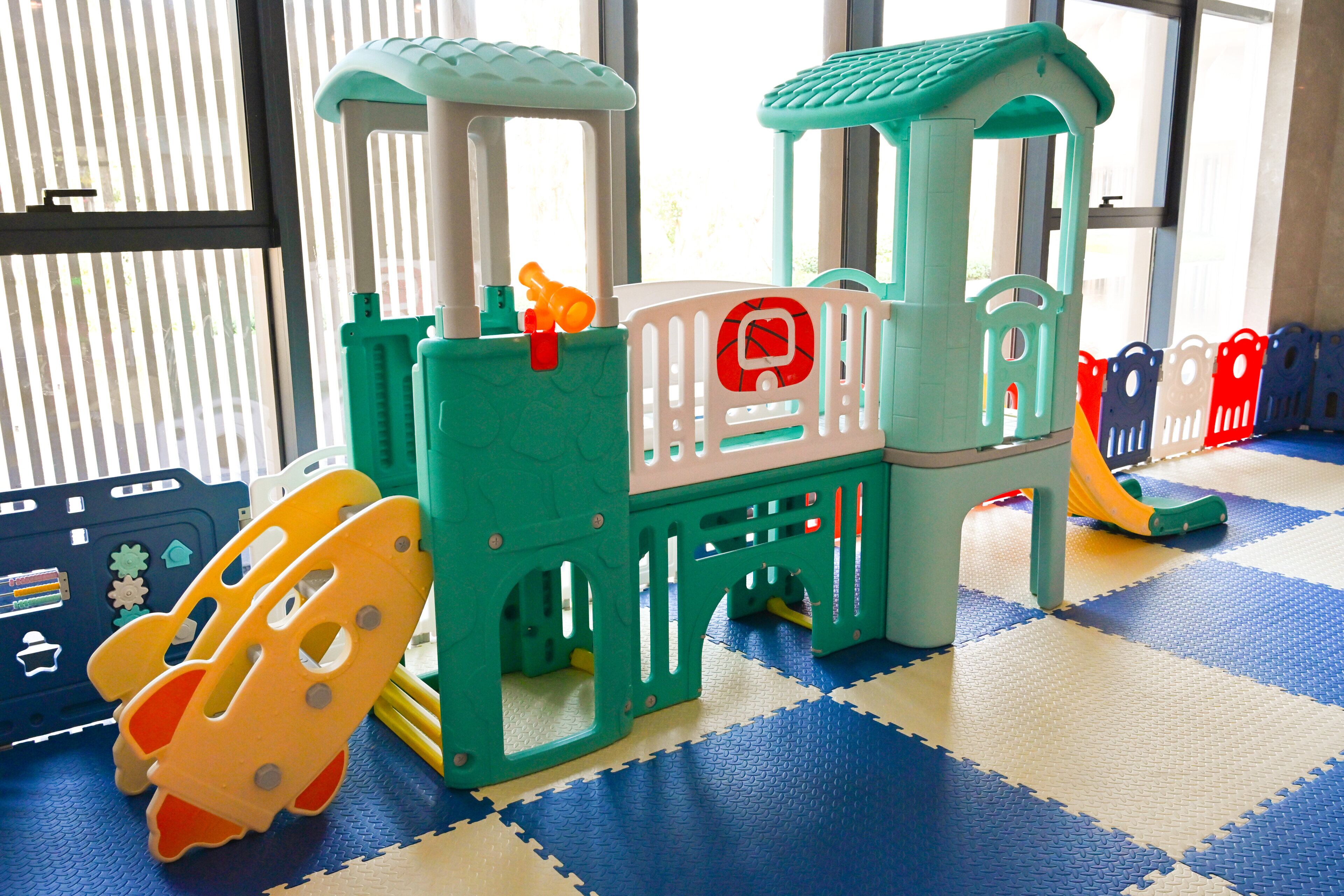 A children's play area with a play structure, a slide, and interlocking foam mats.