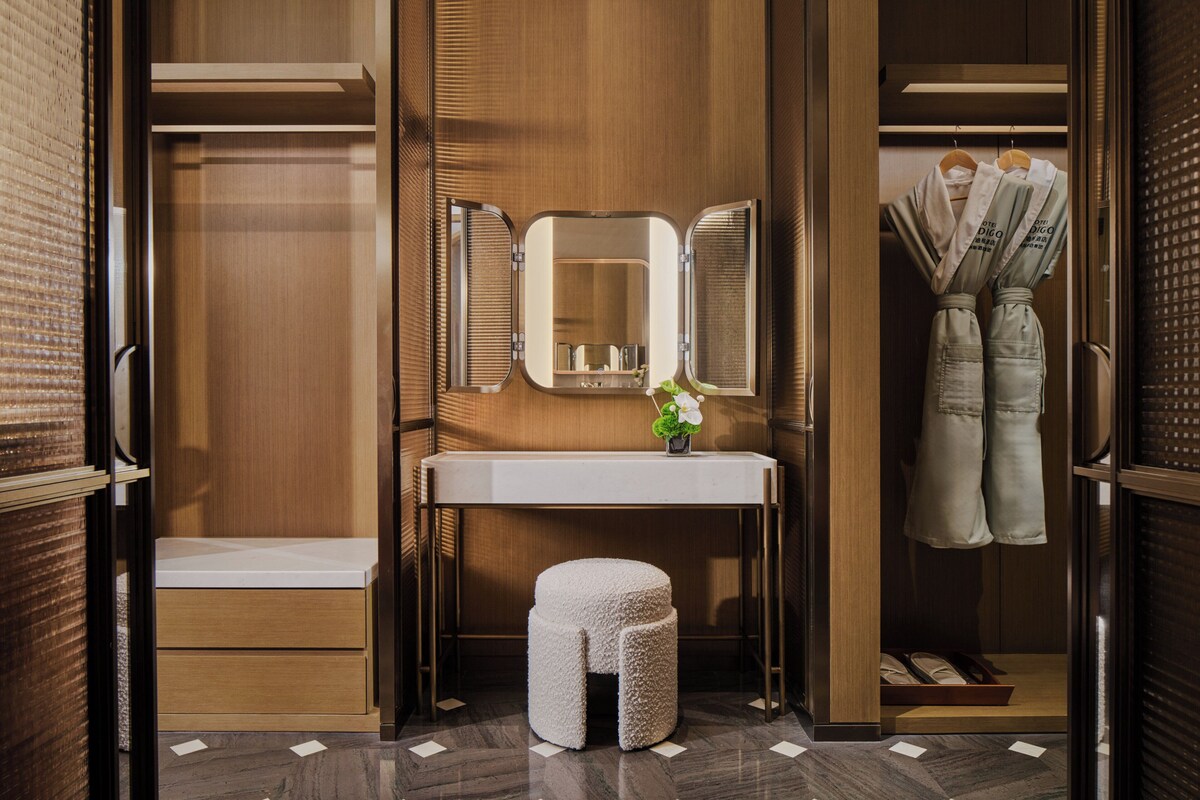 Un dressing avec un coin coiffeuse, un miroir, un petit tabouret et des vêtements suspendus.