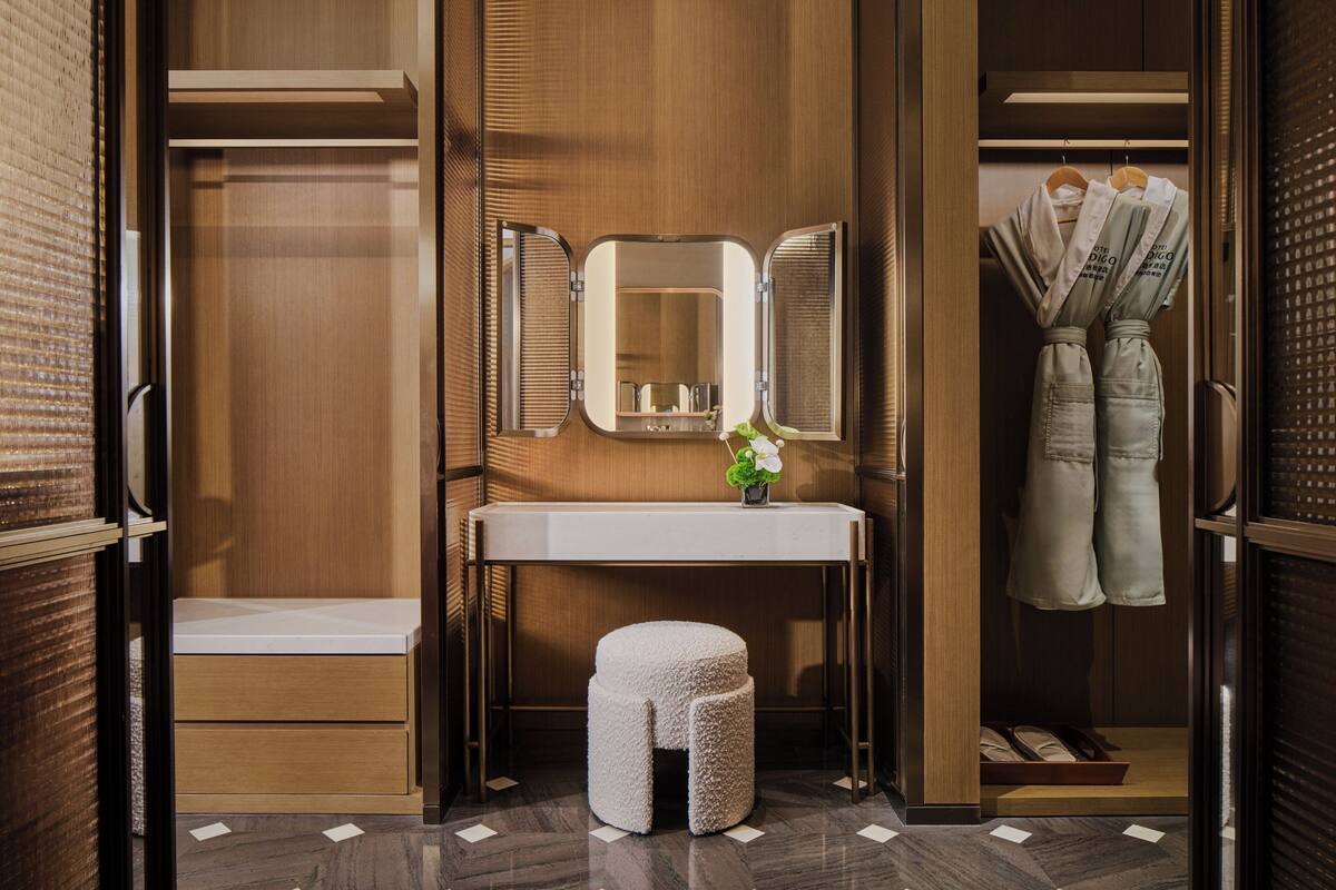 Un dressing avec un coin coiffeuse, un miroir, un petit tabouret et des vêtements suspendus.