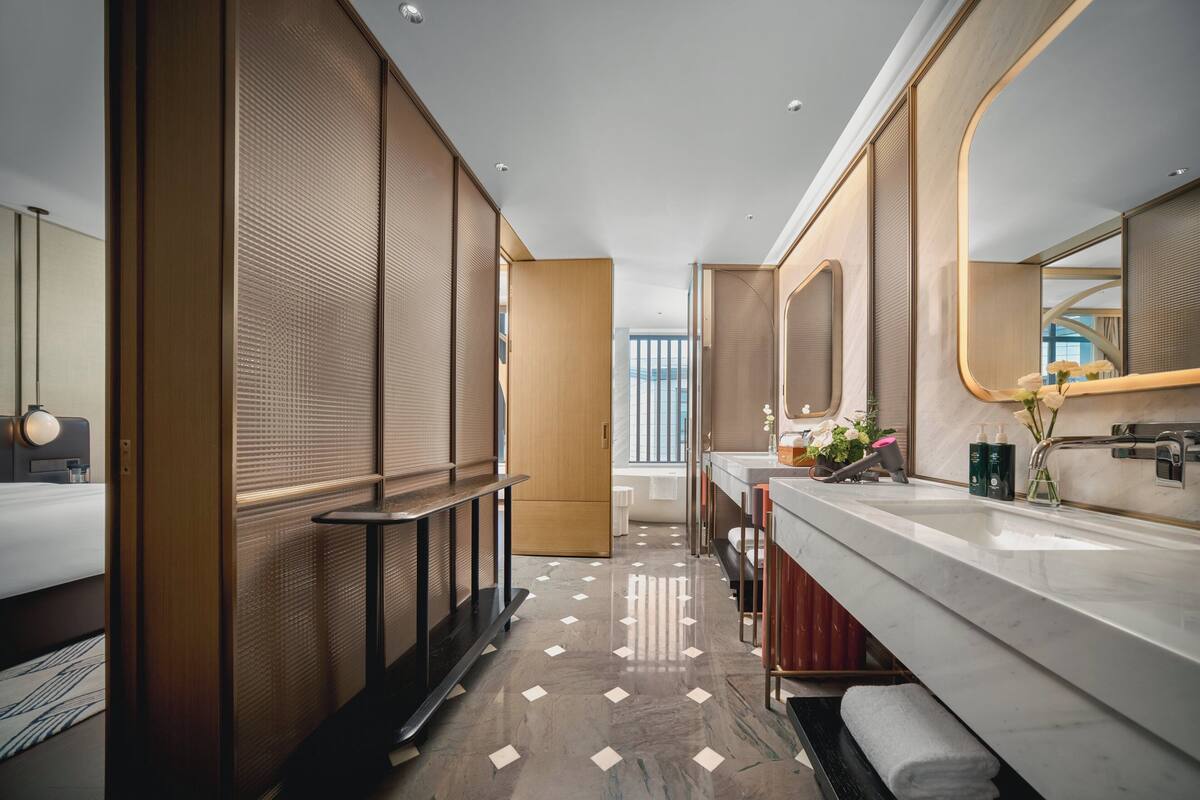 Une salle de bain d’hôtel moderne, dotée d’un grand miroir, d’un meuble-lavabo avec un plan de travail en marbre et d’un espace douche séparé.