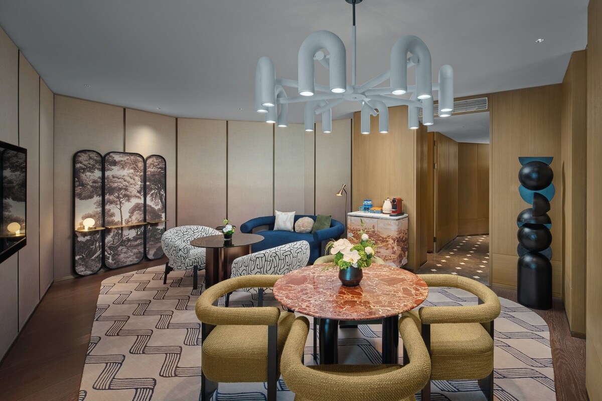 Un hall d’hôtel moderne avec une table ronde en marbre, un tapis à motifs et un canapé bleu.