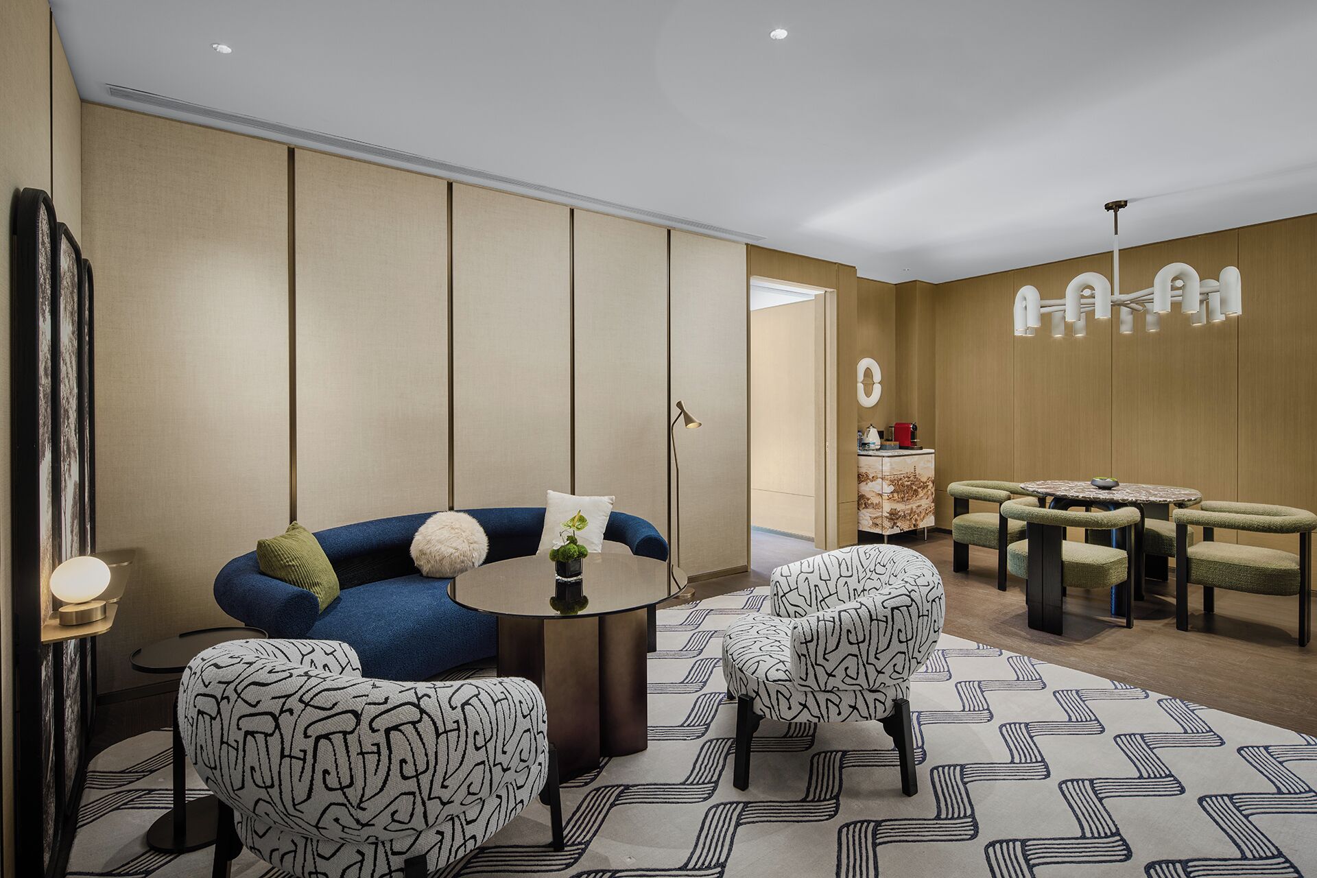 A modern hotel lobby with a sofa, chairs, a round table, and a decorative wall.