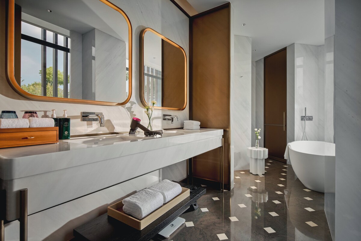 Une salle de bain moderne avec un grand miroir, une baignoire et un meuble-lavabo doté d’un porte-serviettes.