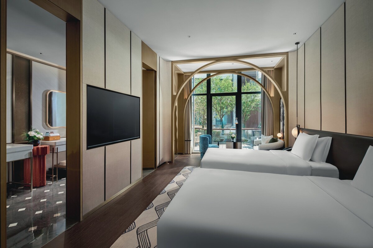 Une chambre d’hôtel moderne dotée d’un grand lit, d’un bureau, d’une télévision à écran plat et d’une grande fenêtre donnant sur l’extérieur.