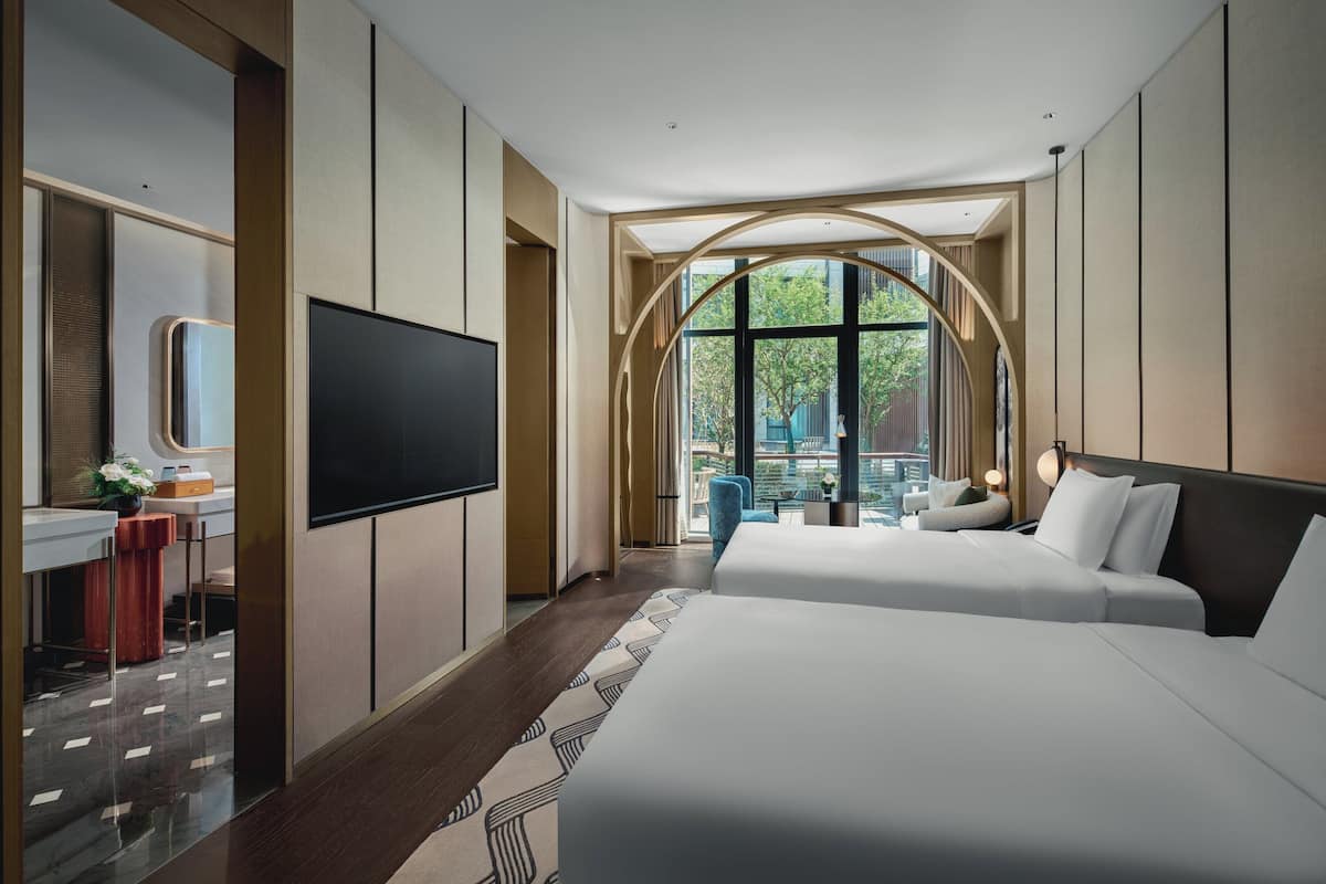 Une chambre d’hôtel moderne dotée d’un grand lit, d’un bureau, d’une télévision à écran plat et d’une grande fenêtre donnant sur l’extérieur.