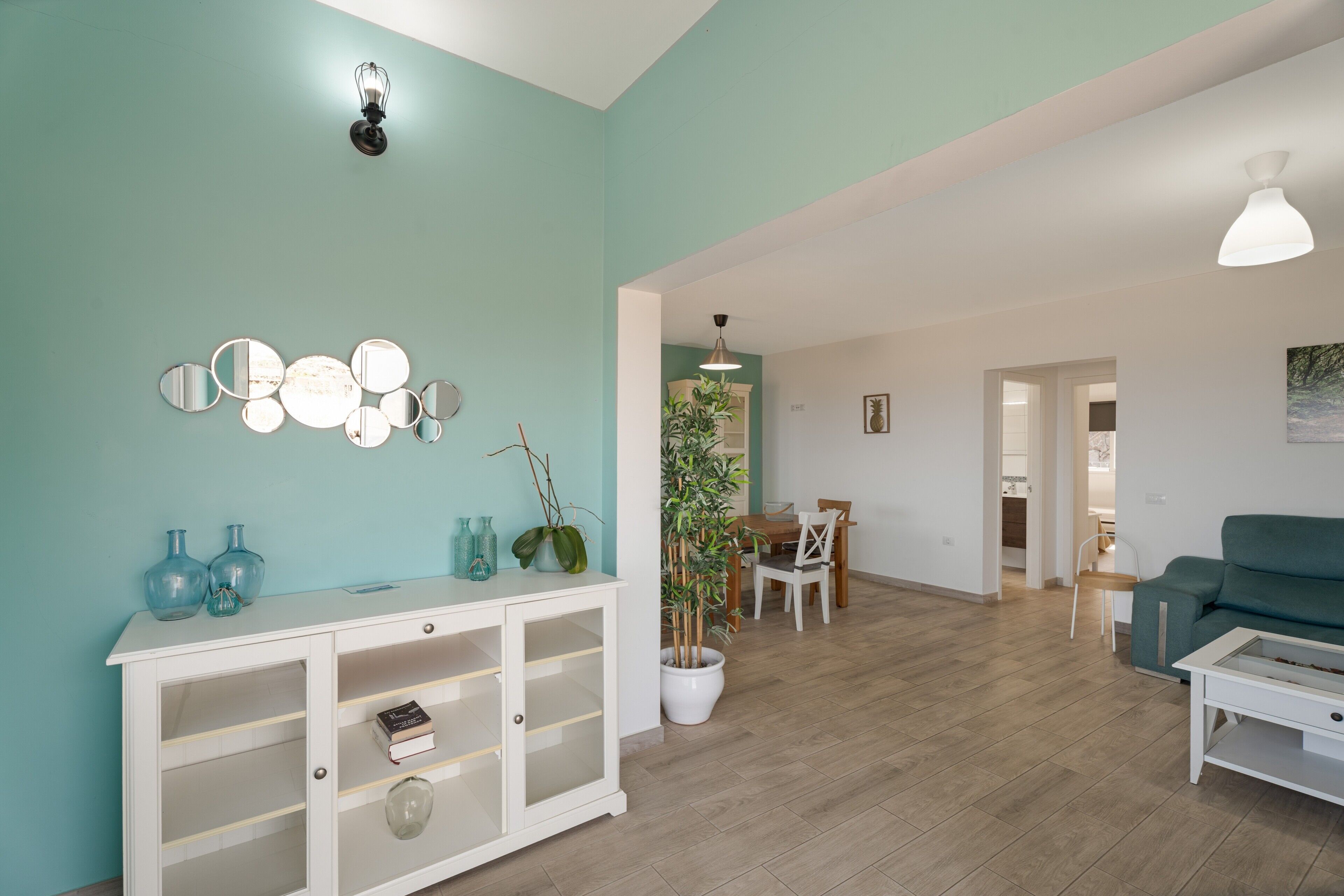 Un salon comprenant un canapé, une table à manger avec des chaises, un meuble blanc avec des étagères et une plante en pot.