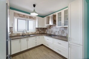 Une cuisine avec des meubles blancs, une fenêtre, un évier et un mur d’accent de couleur turquoise.