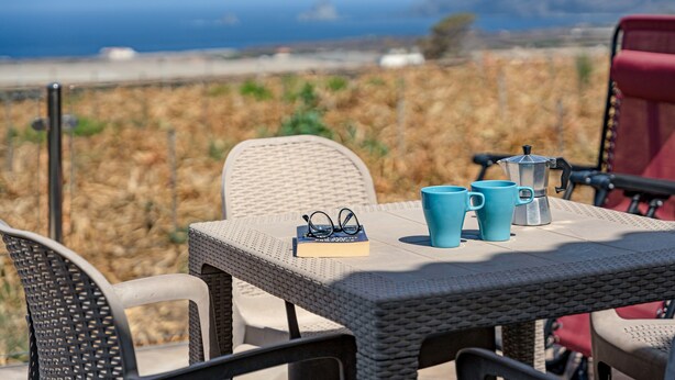 A wicker table with a book, glasses, and two blue mugs, overlooking a beach and mountains. - Holiday Home 'Elvira' with Sea View, Private Terrace and Wi-Fi (La Frontera)