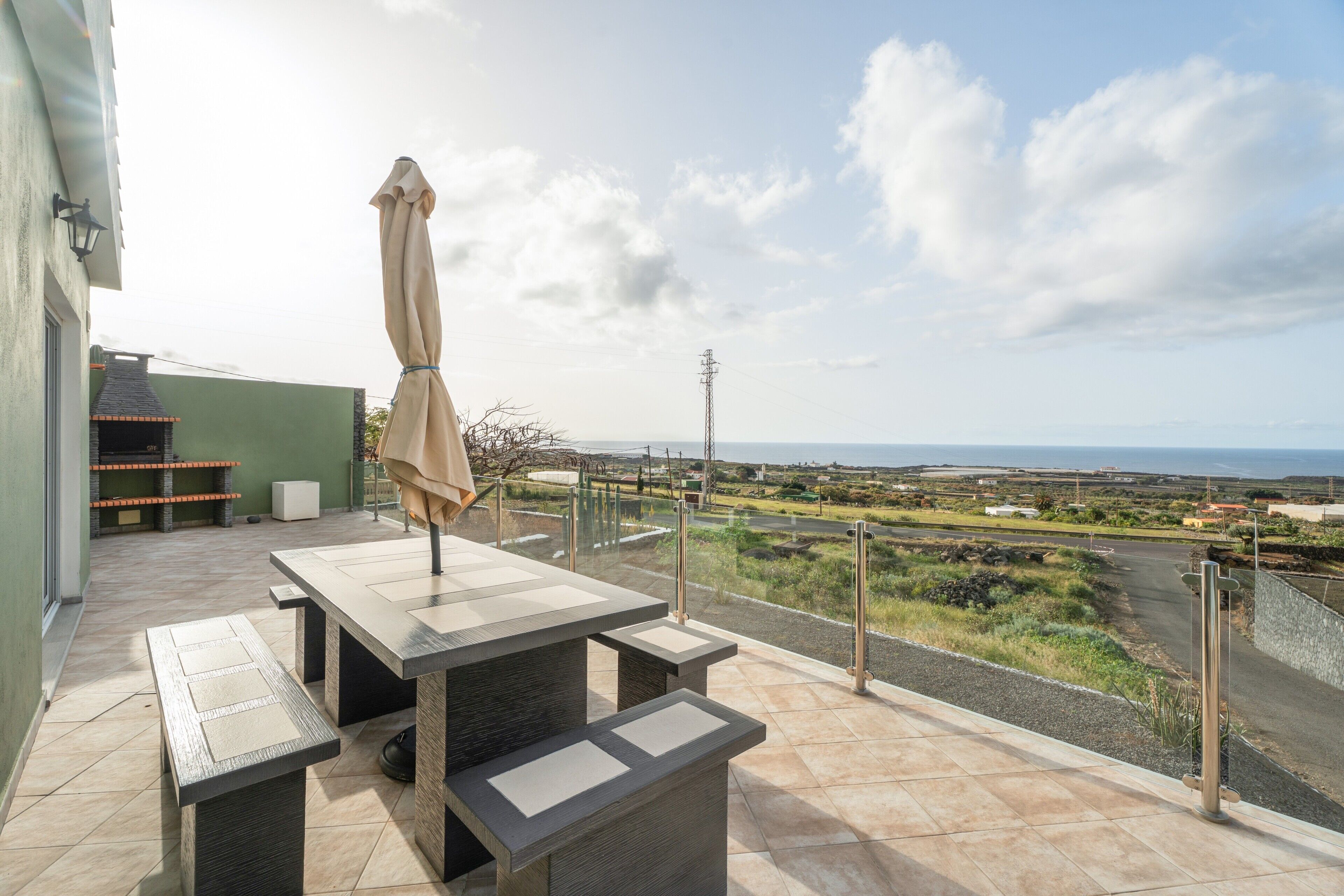 Una terraza con una mesa y bancos, con vistas a un paisaje que incluye una carretera y colinas lejanas.