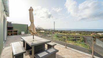 Una terraza con una mesa y bancos, con vistas a un paisaje que incluye una carretera y colinas lejanas.