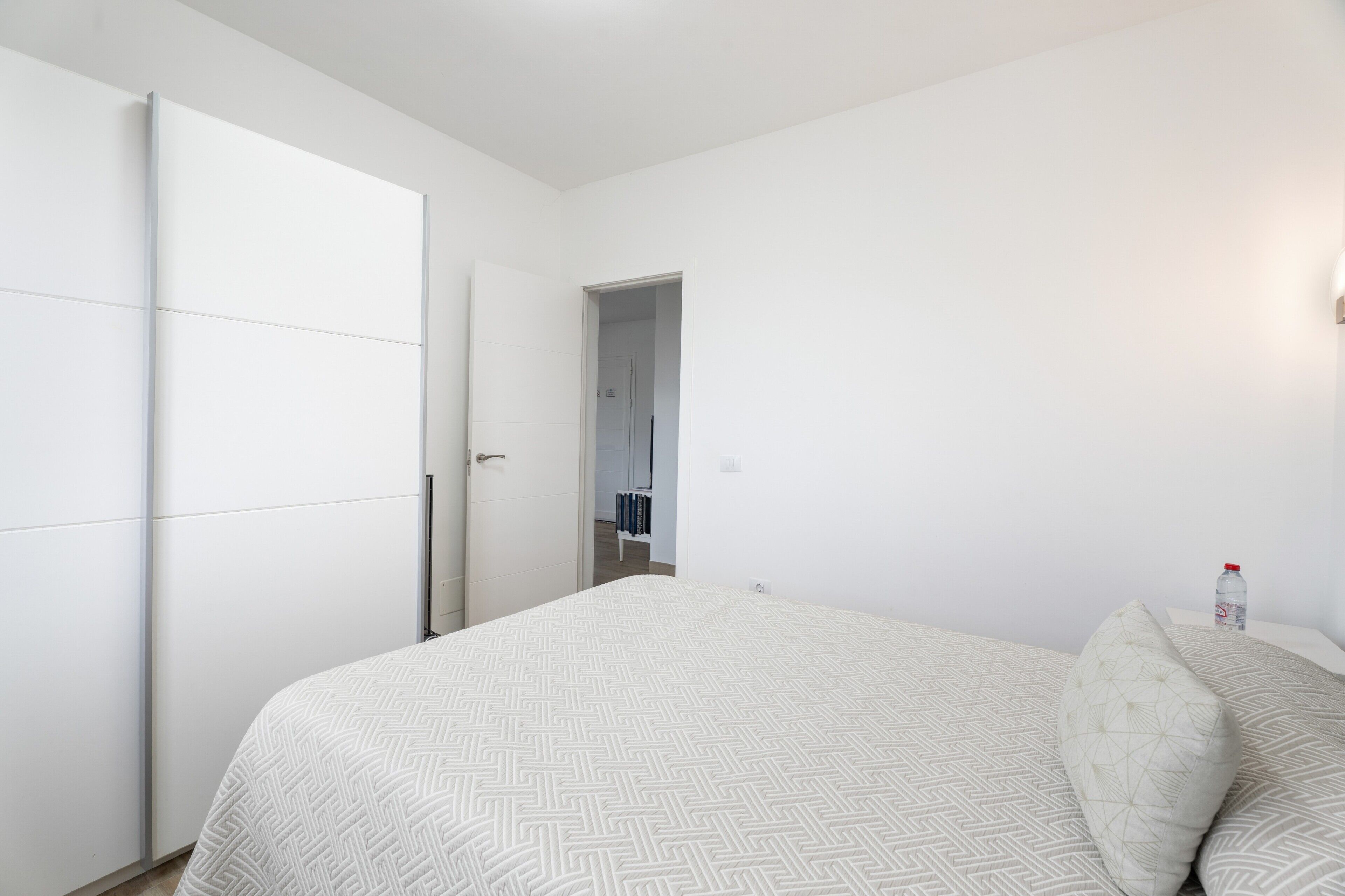 Ein Schlafzimmer mit Bett, Kleiderschrank und Nachttisch mit einer Flasche.