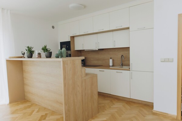 A modern kitchen with white cabinets, a wooden island, and a herringbone floor pattern.