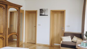 A bedroom with a large bed, a wooden wardrobe, a bedside table, and a door leading to another room.