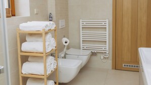 A bathroom with a wooden shelf holding towels, a white bathtub, a white toilet, and a wooden door.