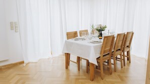 A dining area with a white table set for six, wooden chairs, and a white tablecloth.