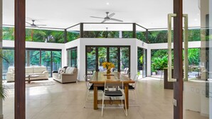 Un interior espacioso y moderno con una zona de comedor central, múltiples opciones de asientos y grandes ventanales con vistas a vegetación exuberante.