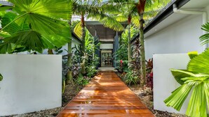 Un sendero bordeado de exuberante vegetación tropical que conduce a un área cubierta con una mesa y sillas.