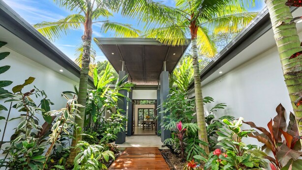 Un edificio moderno con un paseo techado rodeado de exuberante vegetación tropical.