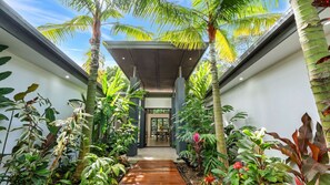 A modern building with a covered walkway surrounded by lush tropical plants. - Villa Vivere (Palm Cove)