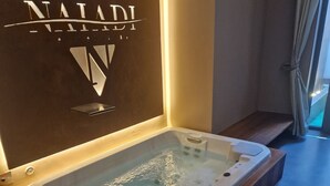 A modern bathroom with a spa tub, a wooden bench, and a wall-mounted sign. - Water lily wellness 5 stars (Caorle)