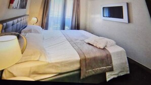 A hotel room with a bed, a TV mounted on the wall, and a window with curtains. - Water lily wellness 5 stars (Caorle)