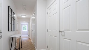 A hallway with white doors, a white table with black legs, and wooden flooring. - Velvet Morning Light For Guests Aged 65s (Surrey)