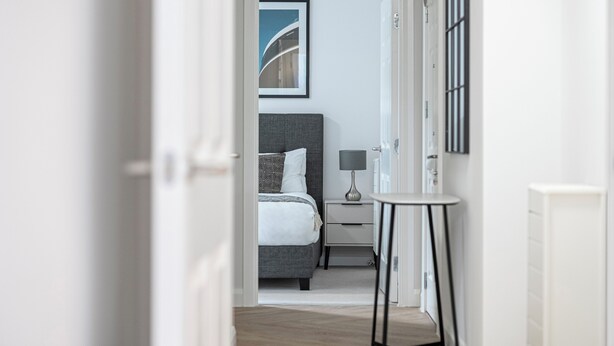 A modern bedroom with a bed, bedside table, lamp, and a framed picture on the wall. - Velvet Morning Light For Guests Aged 65s (Surrey)