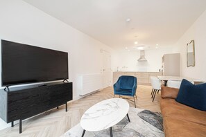 Ett modernt vardagsrum med en stor TV med platt skärm, ett mörkt träskåp, ett soffbord i marmor, en blå fåtölj och en brun soffa.